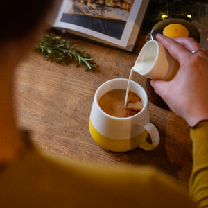 Drinker pouring milk into a tea mug on a wooden table